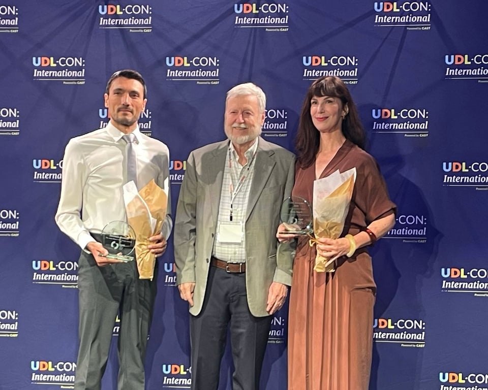 Three people standing together in front of a UDL-CON: International backdrop.